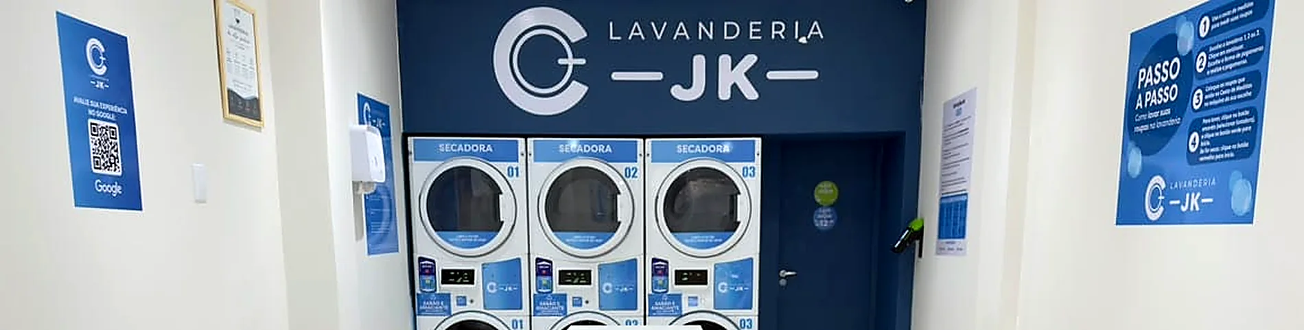 Salão da unidade JK: parede azul com a marca Lavanderia JK e três secadoras numeradas